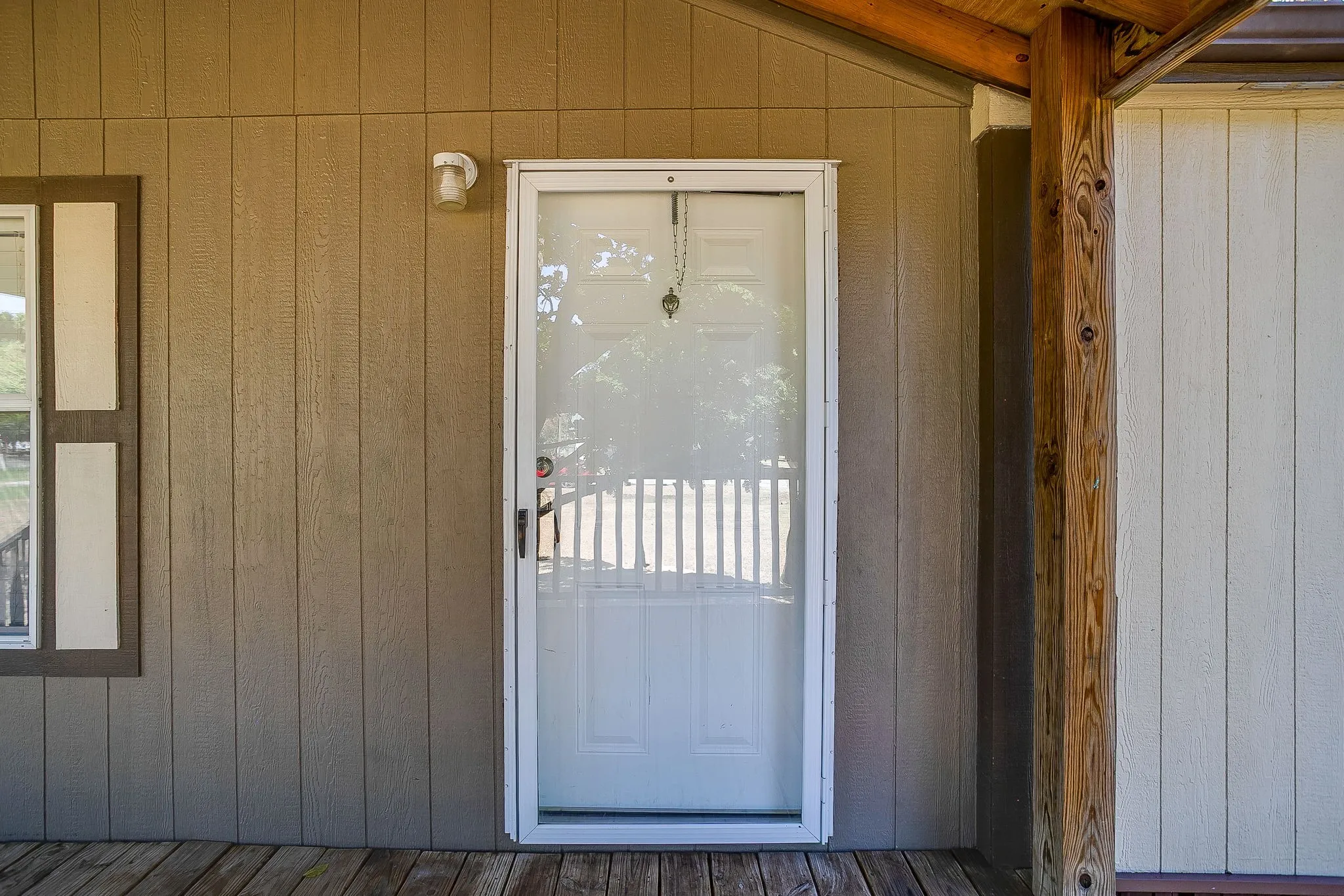 Vertical siding exterior with a storm door entry, wooden porch flooring, and a natural wood support post