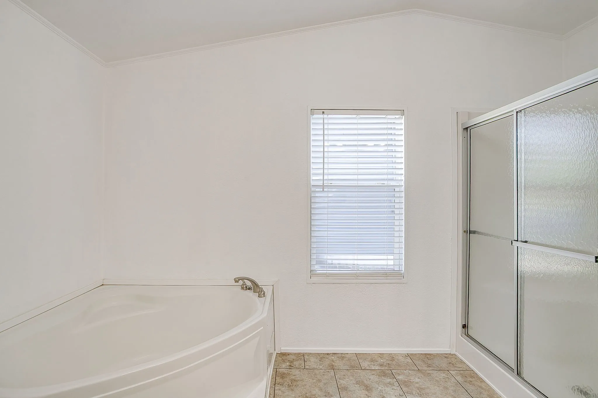 Spacious primary bathroom featuring a curved soaking tub, separate enclosed shower with frameless glass enclosure, neutral tile flooring, and a transom window providing natural light