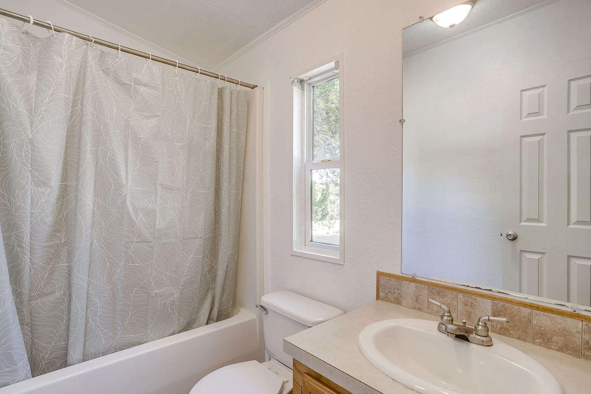 Bright bathroom featuring a ceramic round sink with dual-handle faucet, wood-finish vanity with stone-finish backsplash, and natural light from a tall window