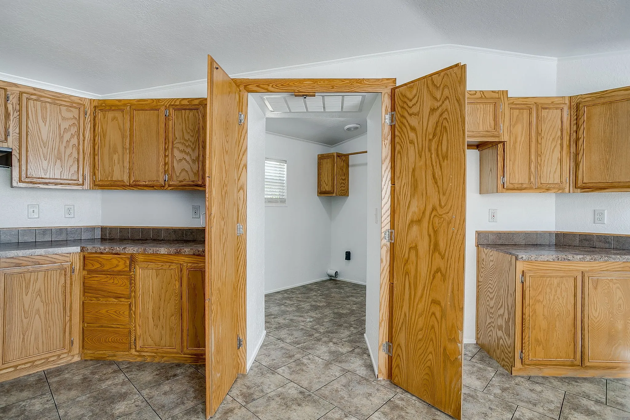 Spacious kitchen featuring warm wood cabinetry throughout, tile flooring, and an open floor plan with generous counter workspace