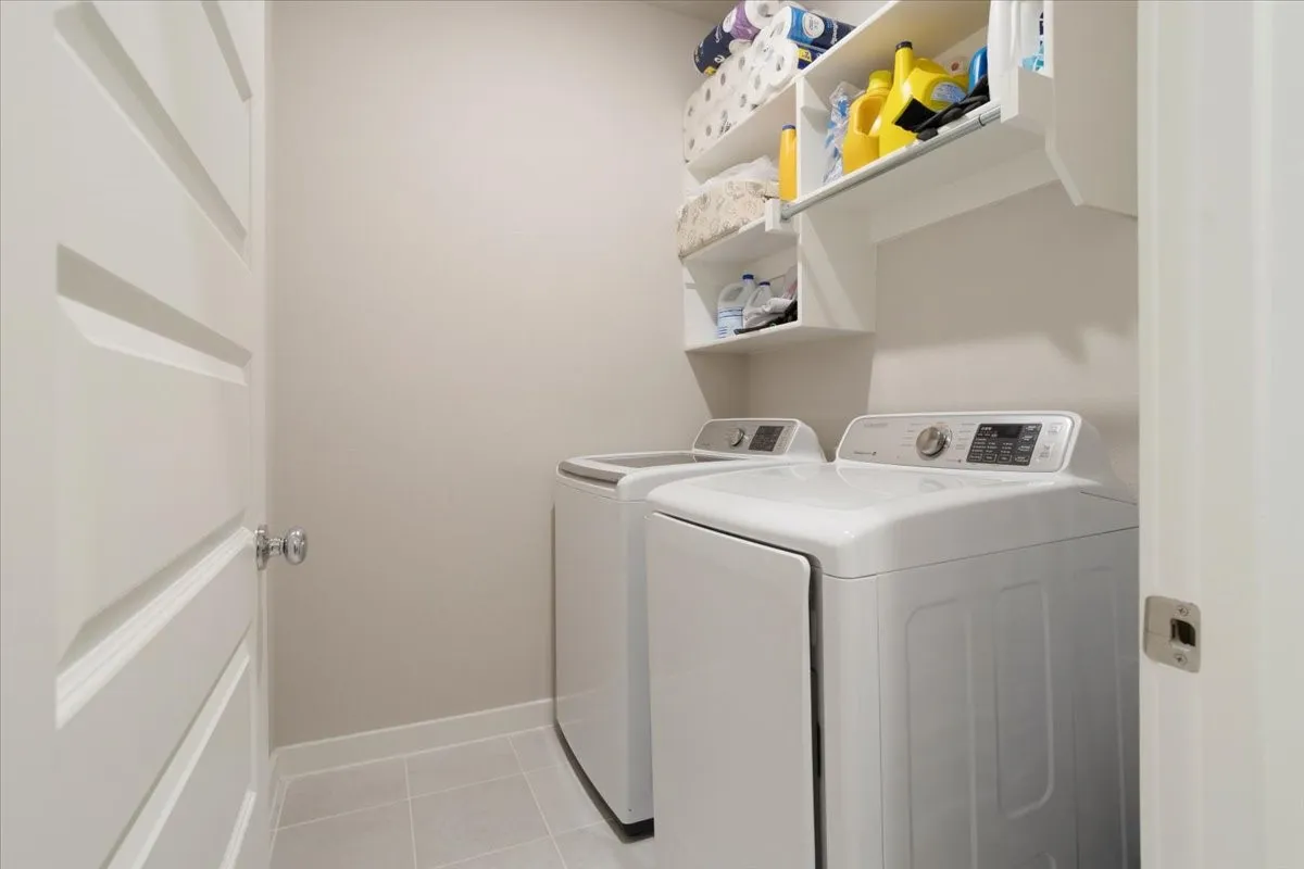 Dedicated laundry area featuring a white top-load washing machine and dryer, built-in shelving, and light-toned tile flooring