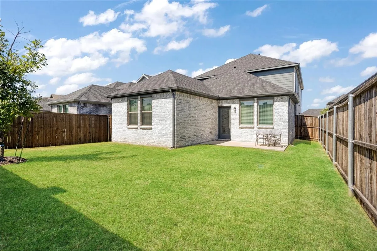 Expansive green lawn with a privacy fence, a brick exterior, and a rear patio