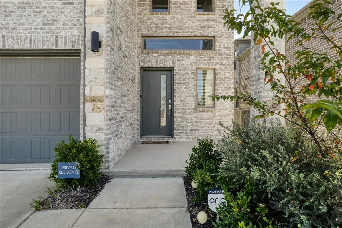 Gray brick and stone facade with a modern front door, horizontal transom window, and vertical accent windows