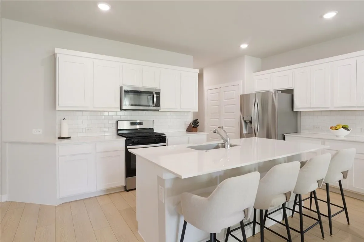 White shaker cabinetry, stainless steel appliances, subway tile backsplash, light wood-finish flooring, and recessed lighting