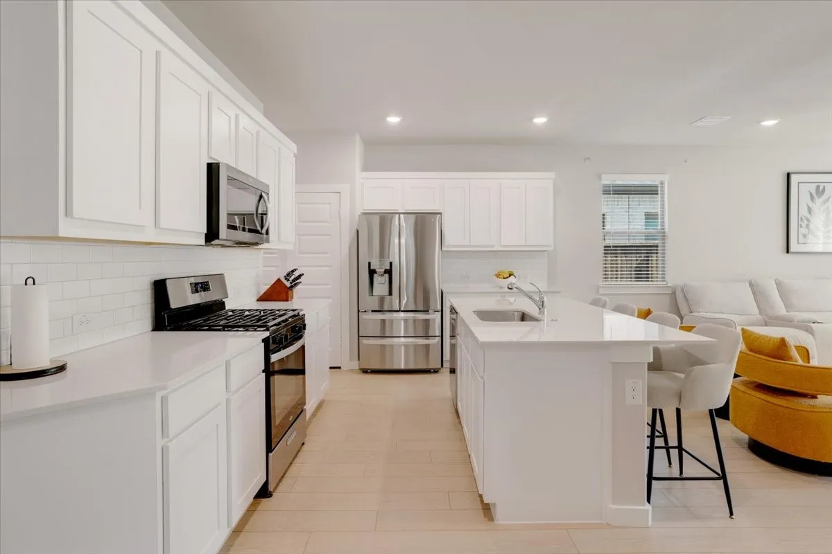 White shaker cabinetry, stainless steel appliances, white subway tile backsplash, light wood-finish flooring, and an island with an integrated sink