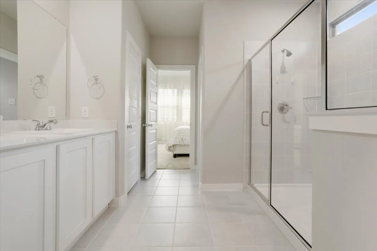 Tile flooring, dual sinks, frameless glass shower enclosure, and a tiled shower surround