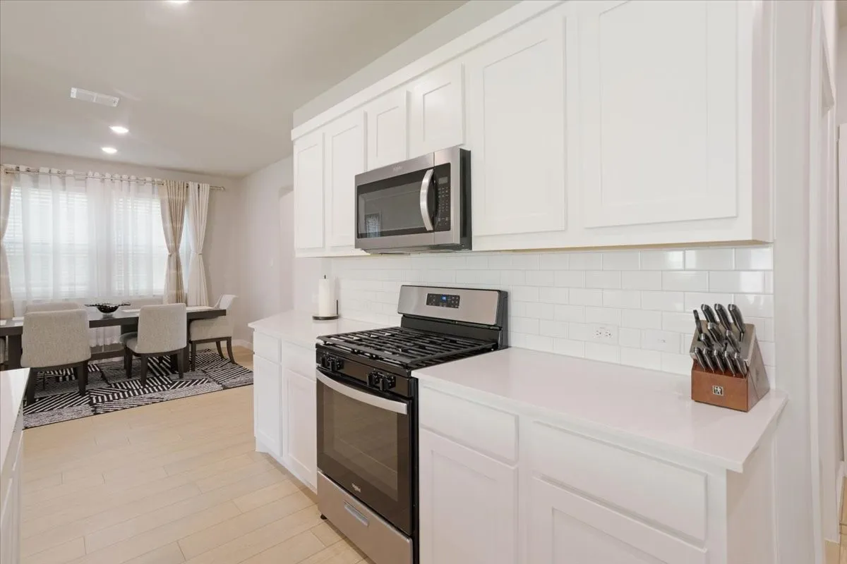White cabinetry, subway tile backsplash, stainless steel appliances, light-toned wood-finish flooring, and recessed lighting