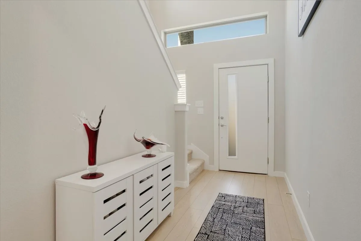 Bright, light-filled entryway featuring a skylight, white painted door with glass panel, light wood-finish flooring
