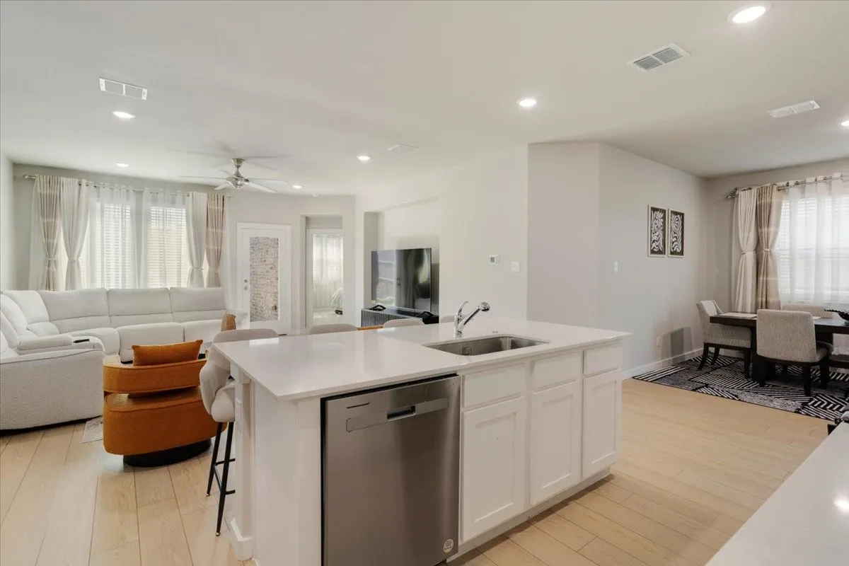 Open-concept living space featuring wood-finish flooring, recessed lighting, and a kitchen island with sink and stainless steel dishwasher