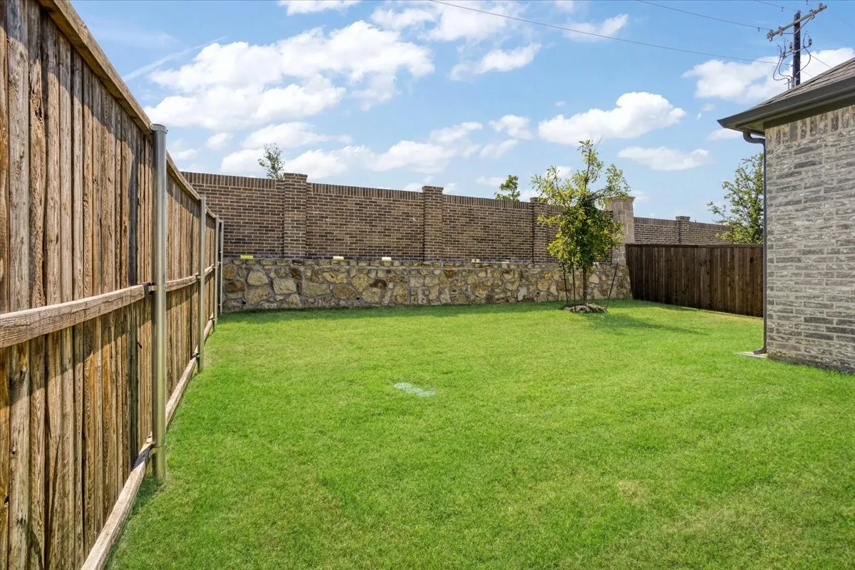 Expansive grassy area with a wood-plank privacy fence, stone and brick retaining wall, and a grey brick exterior