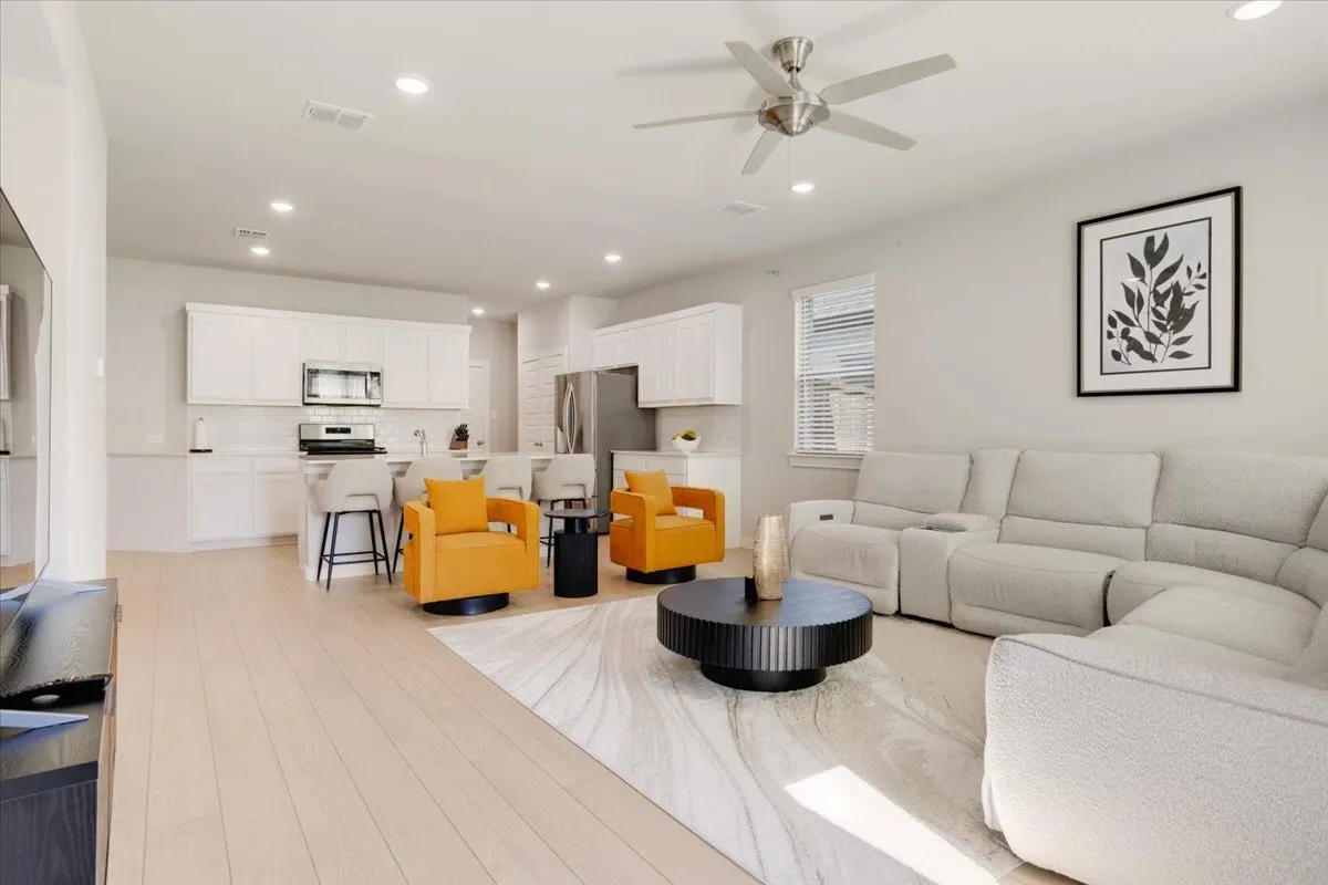 Open-concept living space featuring wood-finish flooring, recessed lighting, a ceiling fan, and white kitchen cabinetry with stainless steel appliances