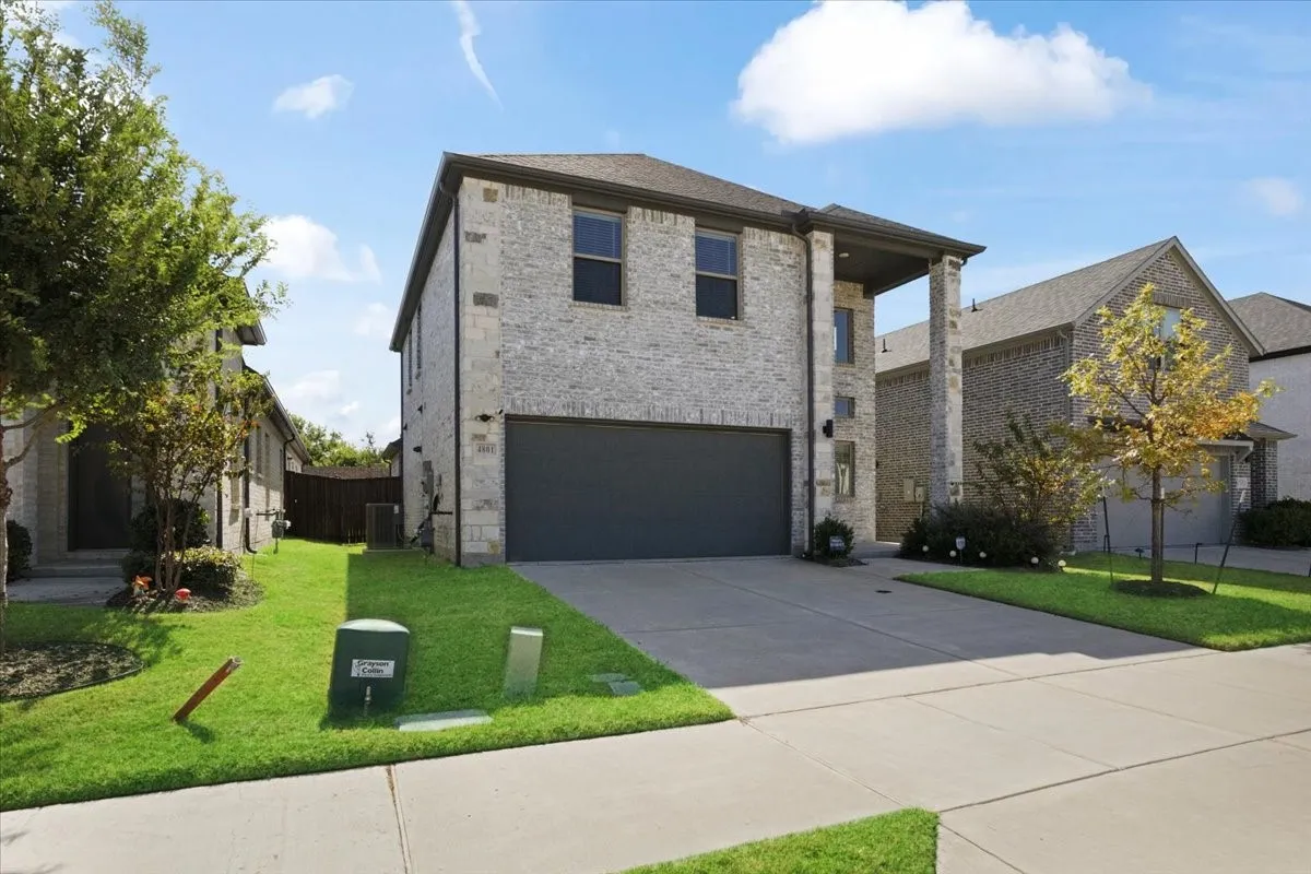 Two-story residence featuring a light-colored brick exterior, a dark-toned garage door, and a concrete driveway