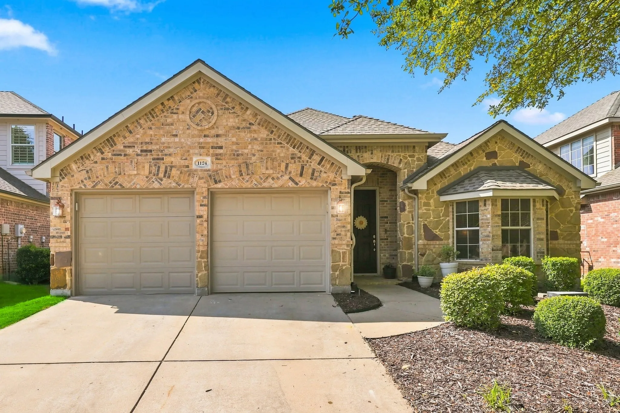 Brick and stone facade with a two-car garage, arched entryway, bay window, and manicured landscaping
