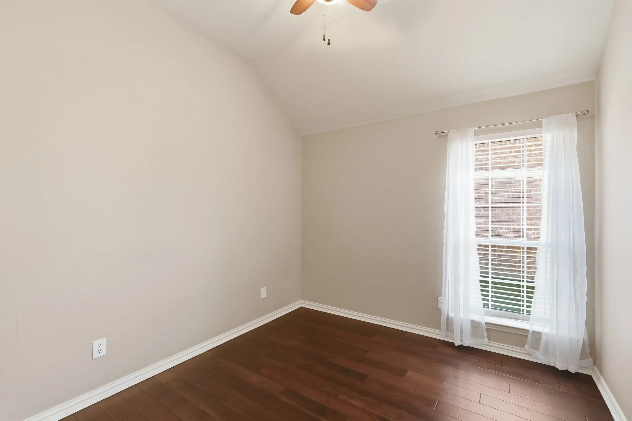 Downstair bedroom.Vaulted ceiling, wood-finish flooring, ceiling fan, window with blinds, and neutral wall paint