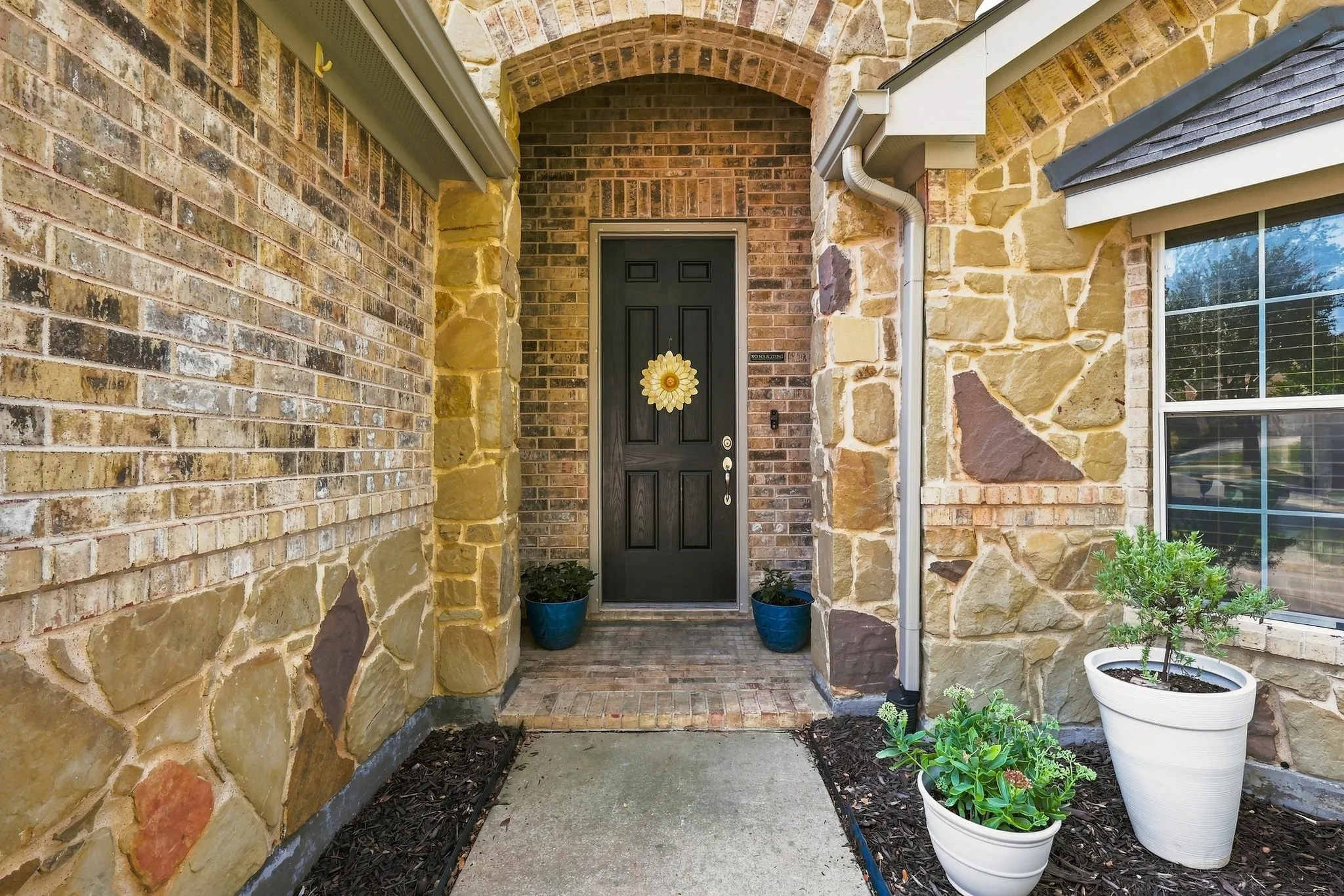 Brick and stone exterior with an arched entryway, dark panel front door, and a multi-pane window