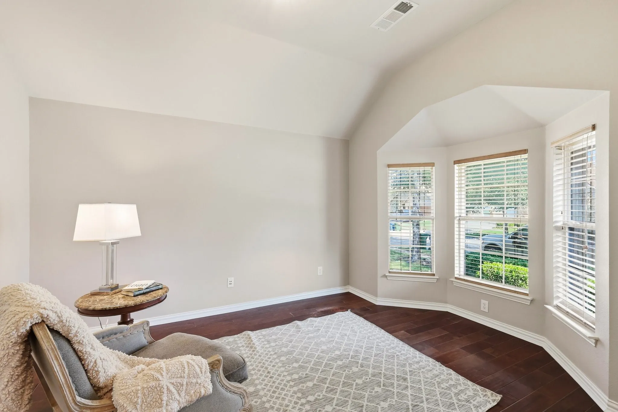 Hardwood flooring, light neutral wall color, vaulted ceiling, three large windows, and a bay window design