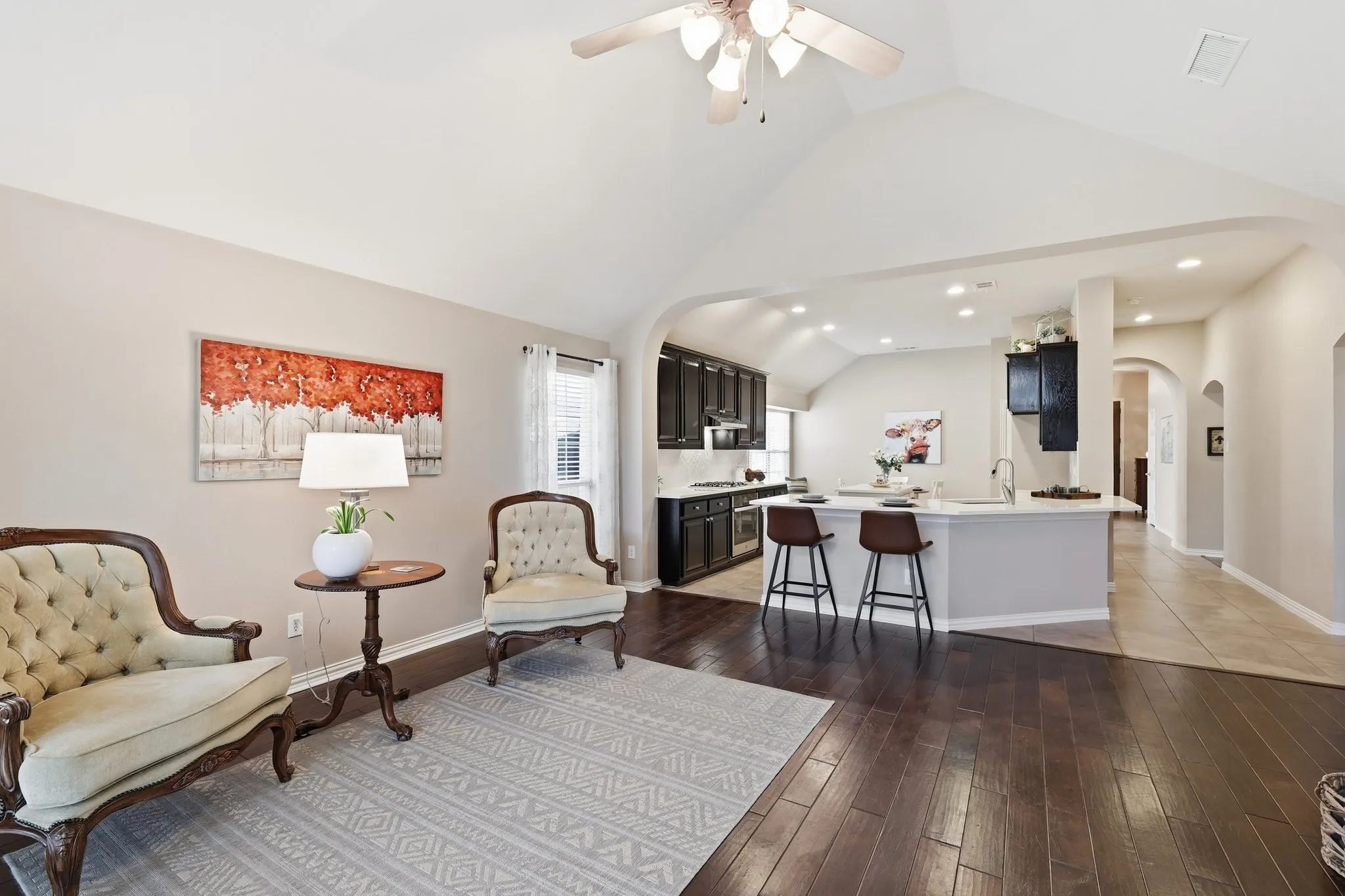 Cathedral ceiling with a ceiling fan, arched transom window, wood-finish flooring, brick fireplace surround, and multiple windows with blinds