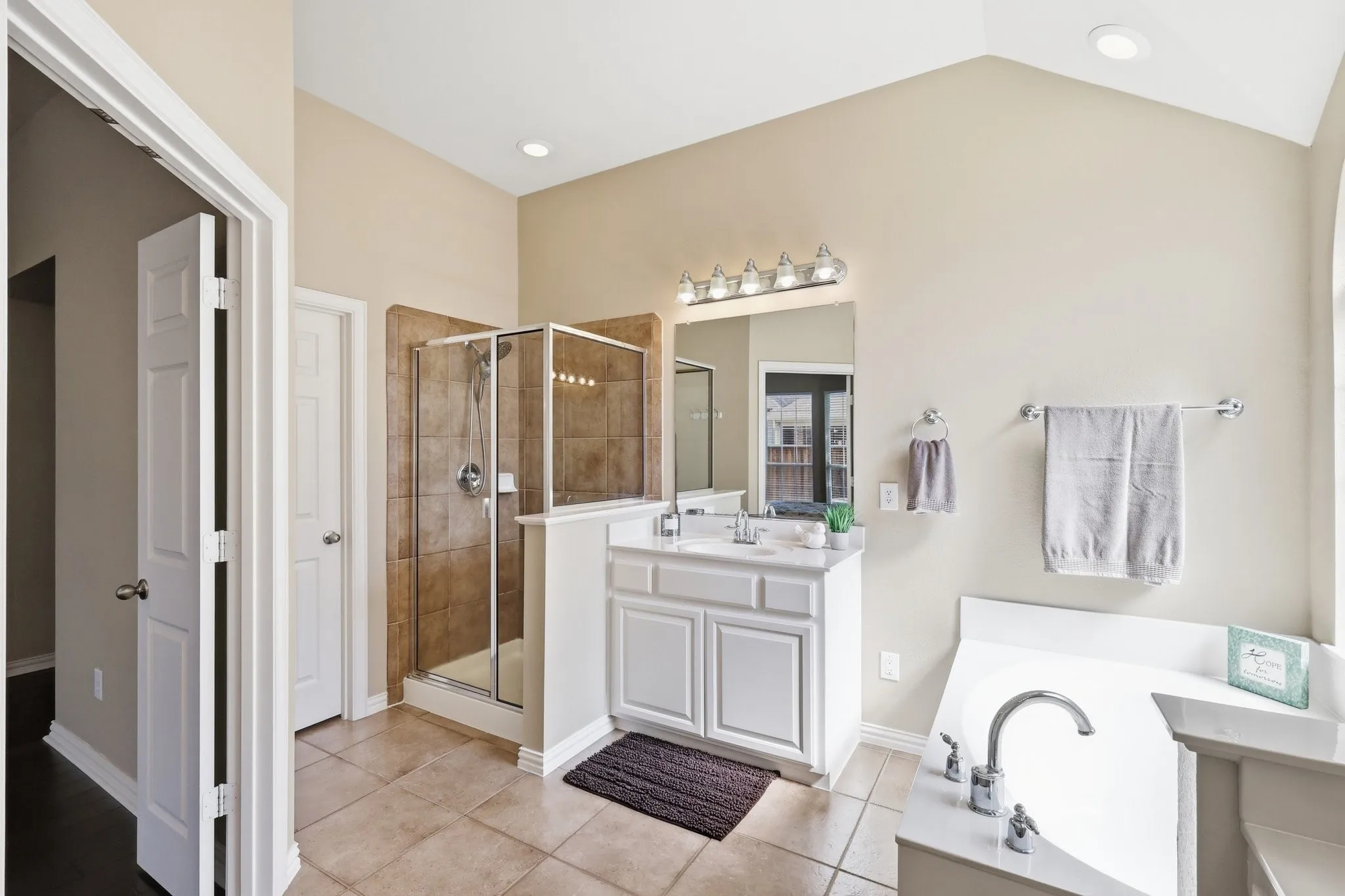 Vaulted ceiling bathroom featuring a glass-enclosed shower with tile surround, a built-in soaking tub, and a vanity with dual sinks