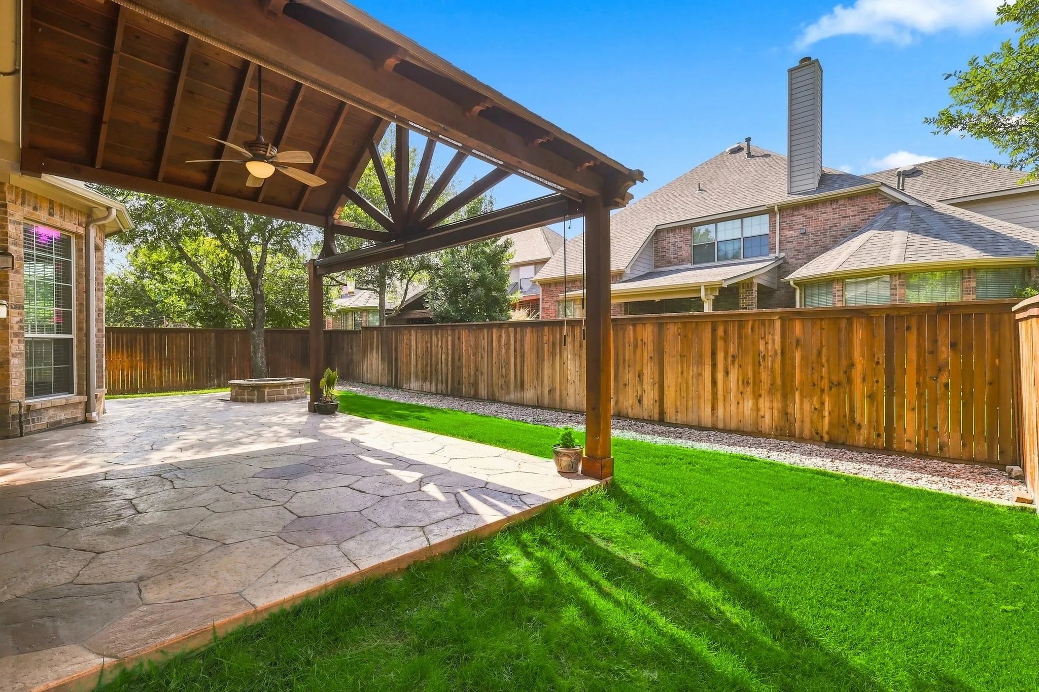 Covered patio featuring a wood-beam ceiling with an integrated ceiling fan, a flagstone-style paved surface, and a built-in fire pit