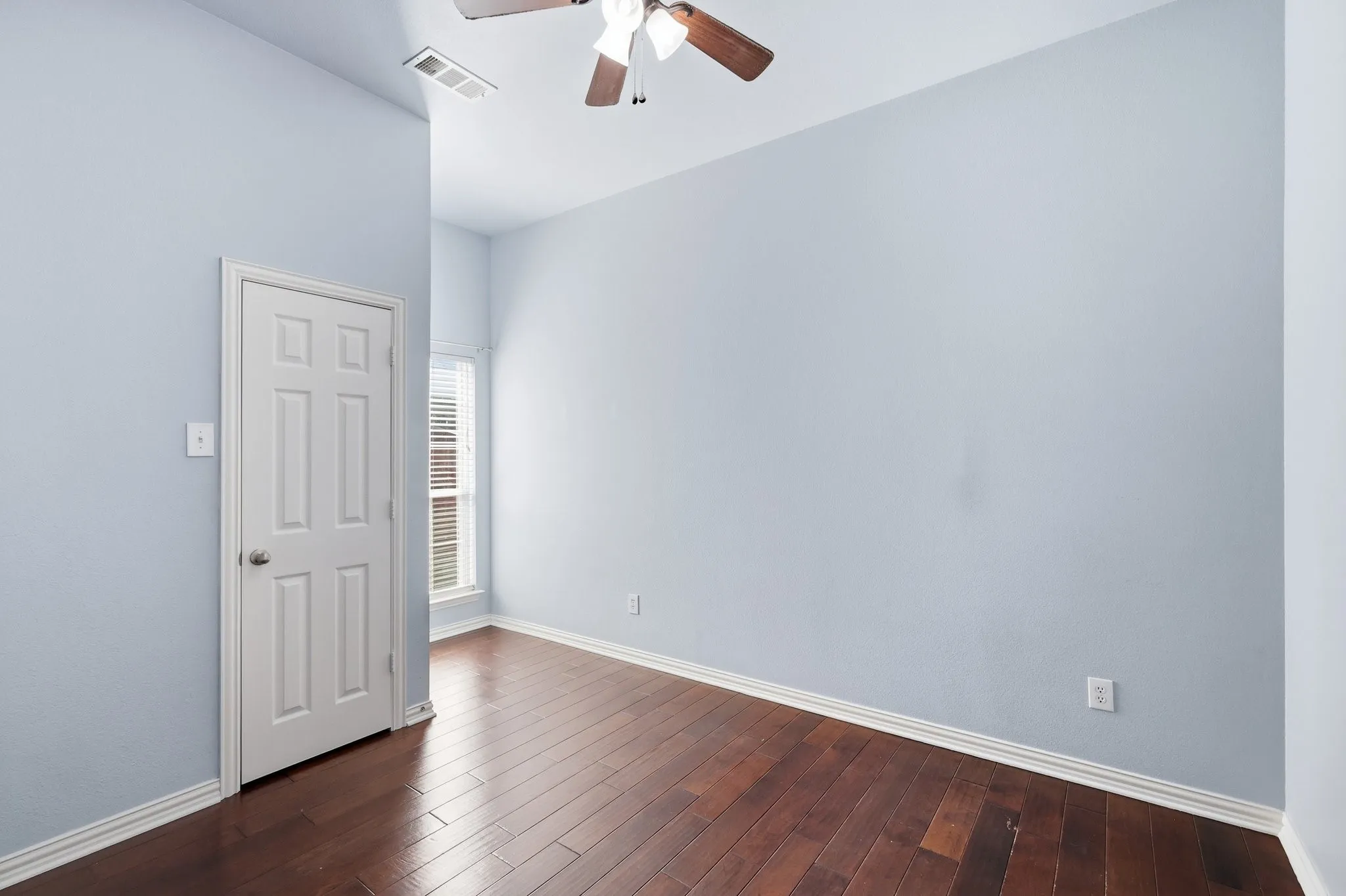 Downstair bedroom. Vaulted ceiling, wood-finish flooring, ceiling fan, window with blinds, and neutral wall paint