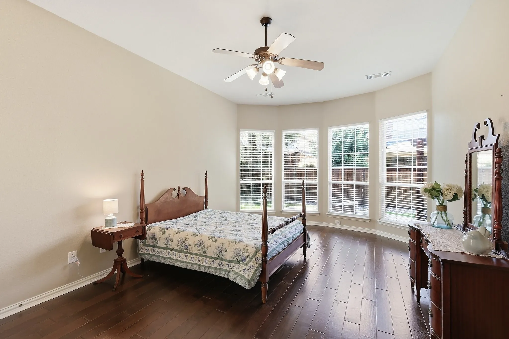 Spacious room featuring wood-finish flooring, a bay window with multiple panes, and a ceiling fan with integrated lighting