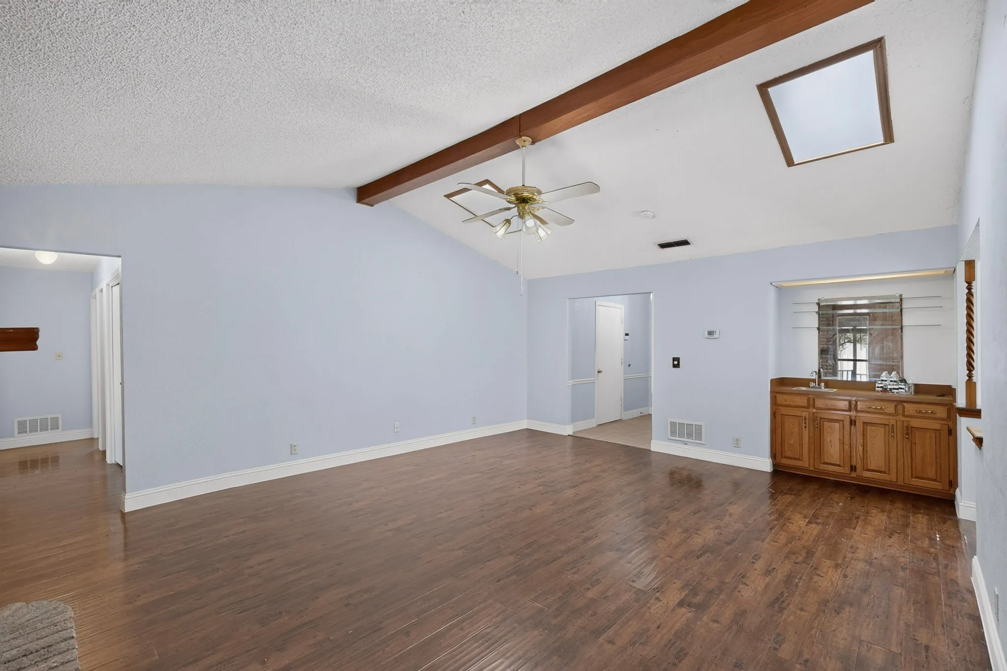 Vaulted ceiling with exposed wood beams, wood-finish flooring, skylight, built-in cabinetry, and a ceiling fan