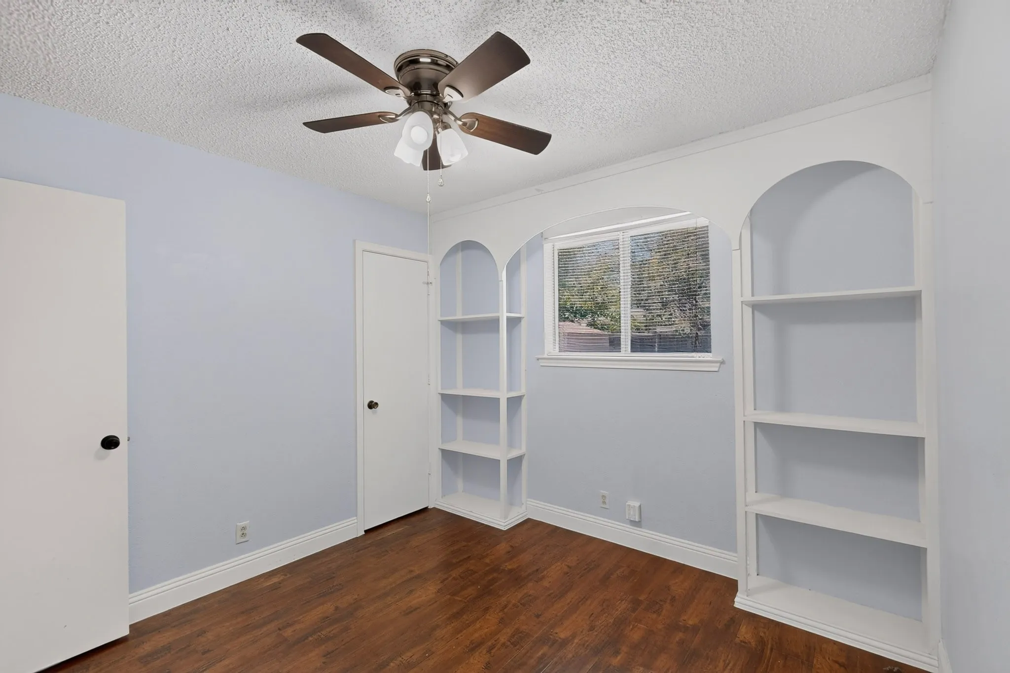 Wood-finish flooring with light-toned walls and white trim with build in Shelves and Ceiling Fan