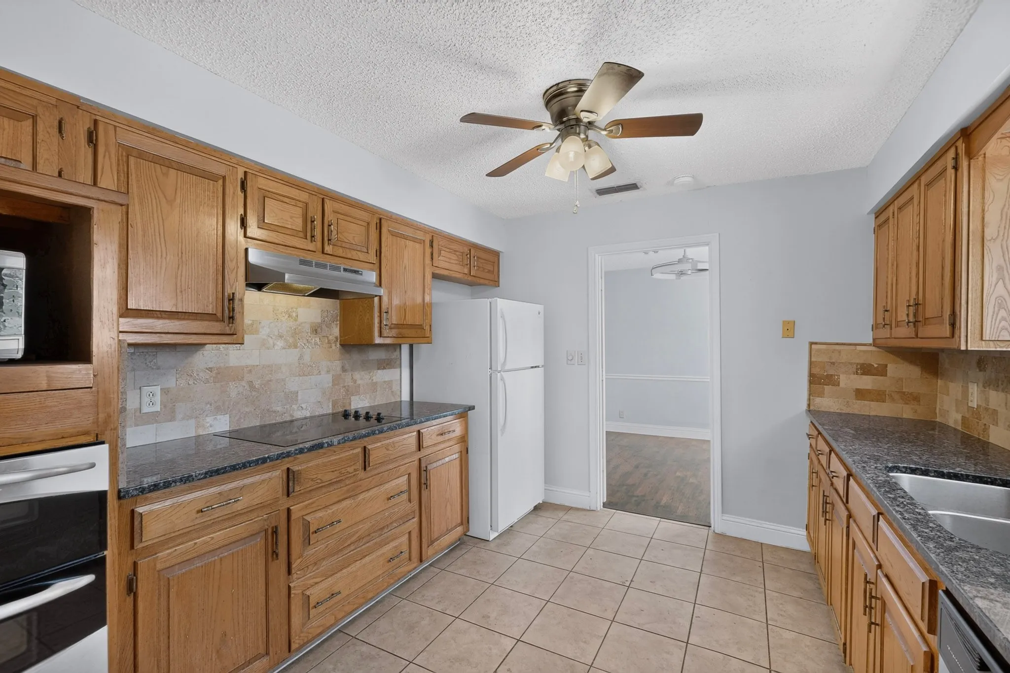 Kitchen featuring wood cabinetry, dark countertops, a tiled backsplash, and ceramic tile flooring