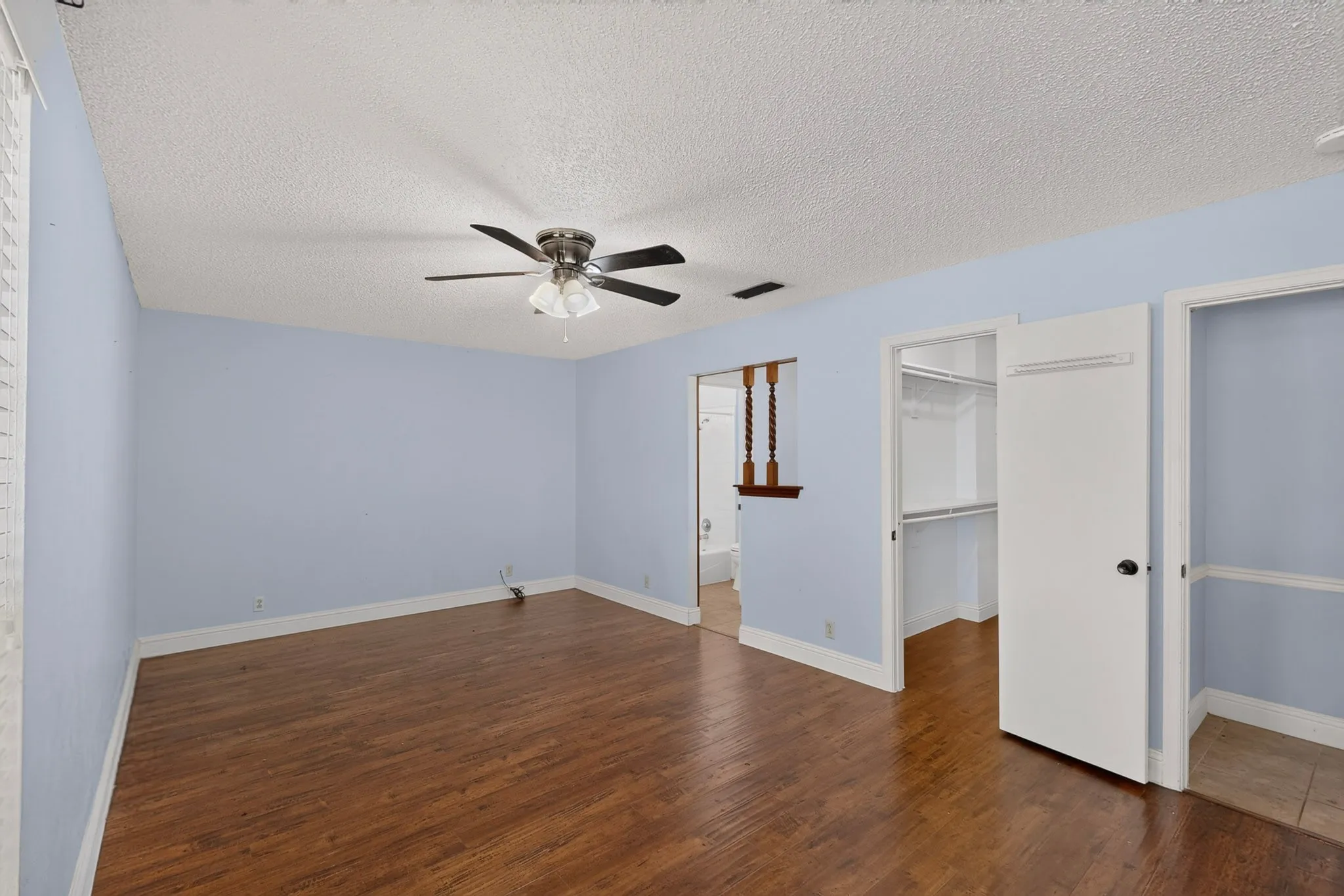 Spacious room featuring wood-finish flooring, a ceiling fan, and an open closet with built-in shelving