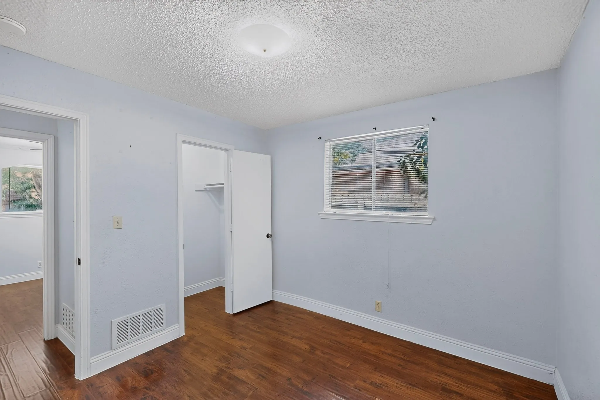 Wood-finish flooring with white trim, a built-in closet with shelving, and a window with blinds