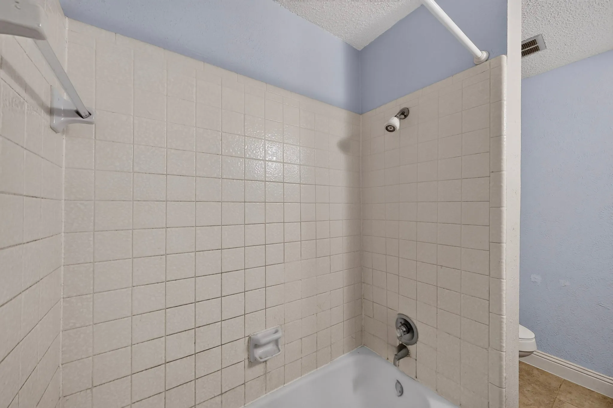 Bathtub with white tile surround, chrome showerhead, and wall-mounted soap dish