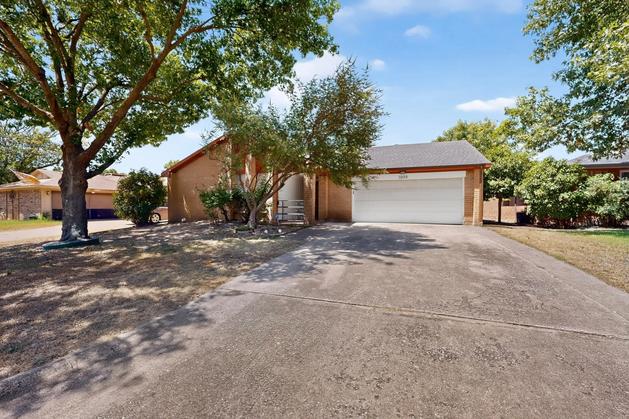 Brick exterior with an attached garage, featuring a concrete driveway and mature trees