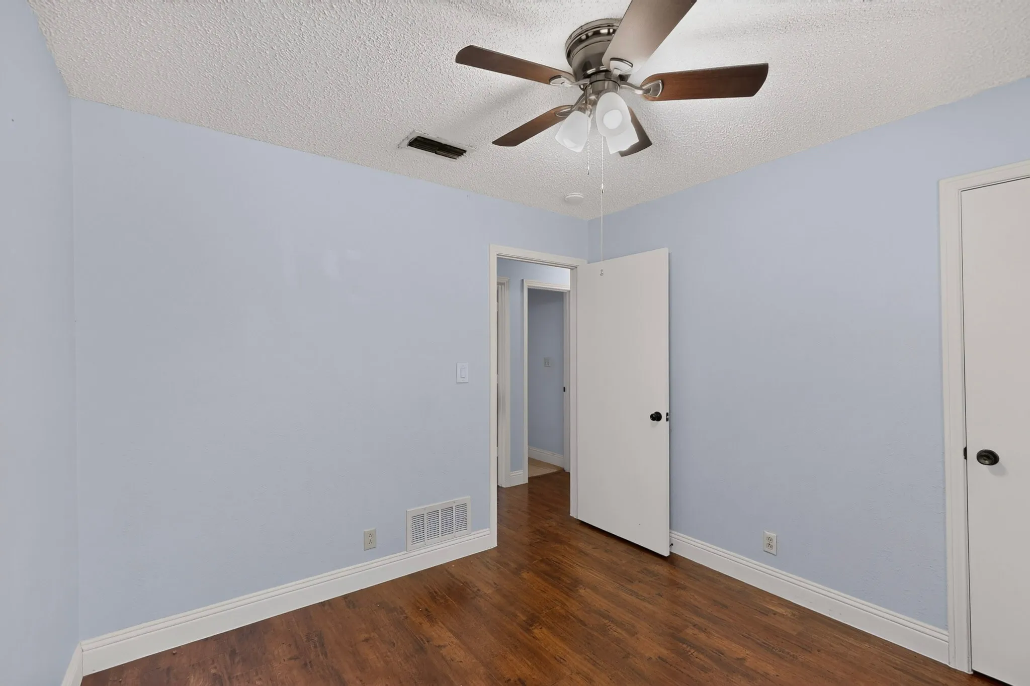 Wood-finish flooring with light-toned walls and white trim, ceiling fan