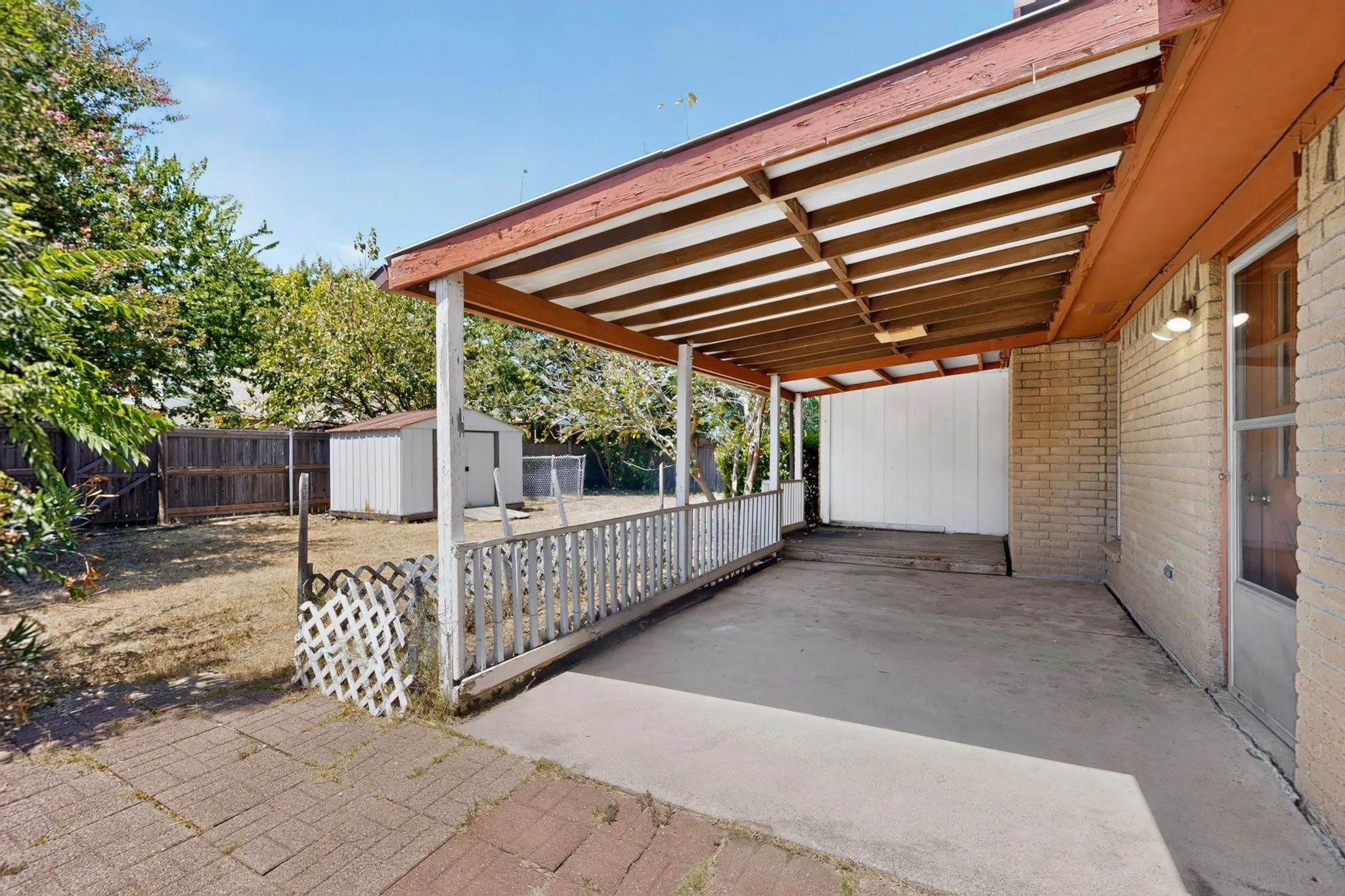 Covered patio with a concrete surface, lattice railing, and brick exterior
