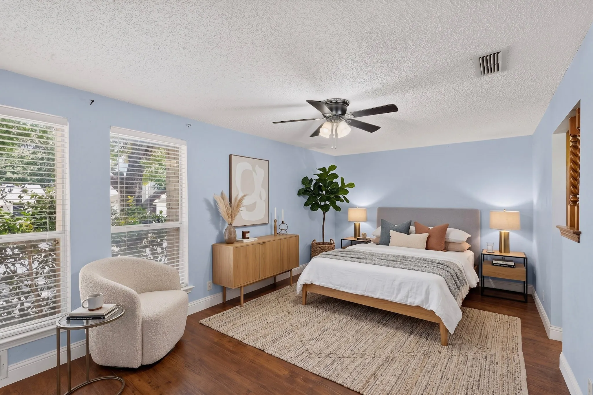 AI Staged  Wood-finish flooring with a neutral area rug, two windows with blinds, and a ceiling fan with integrated lighting
