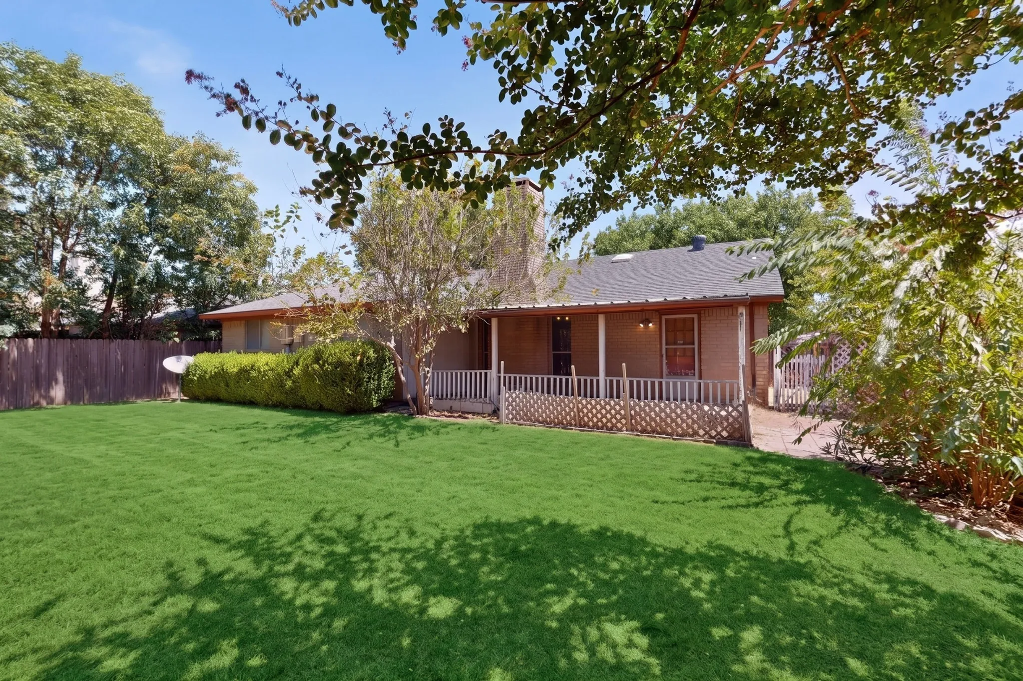 AI
Expansive green lawn, covered patio, brick exterior, wood privacy fence, and mature trees