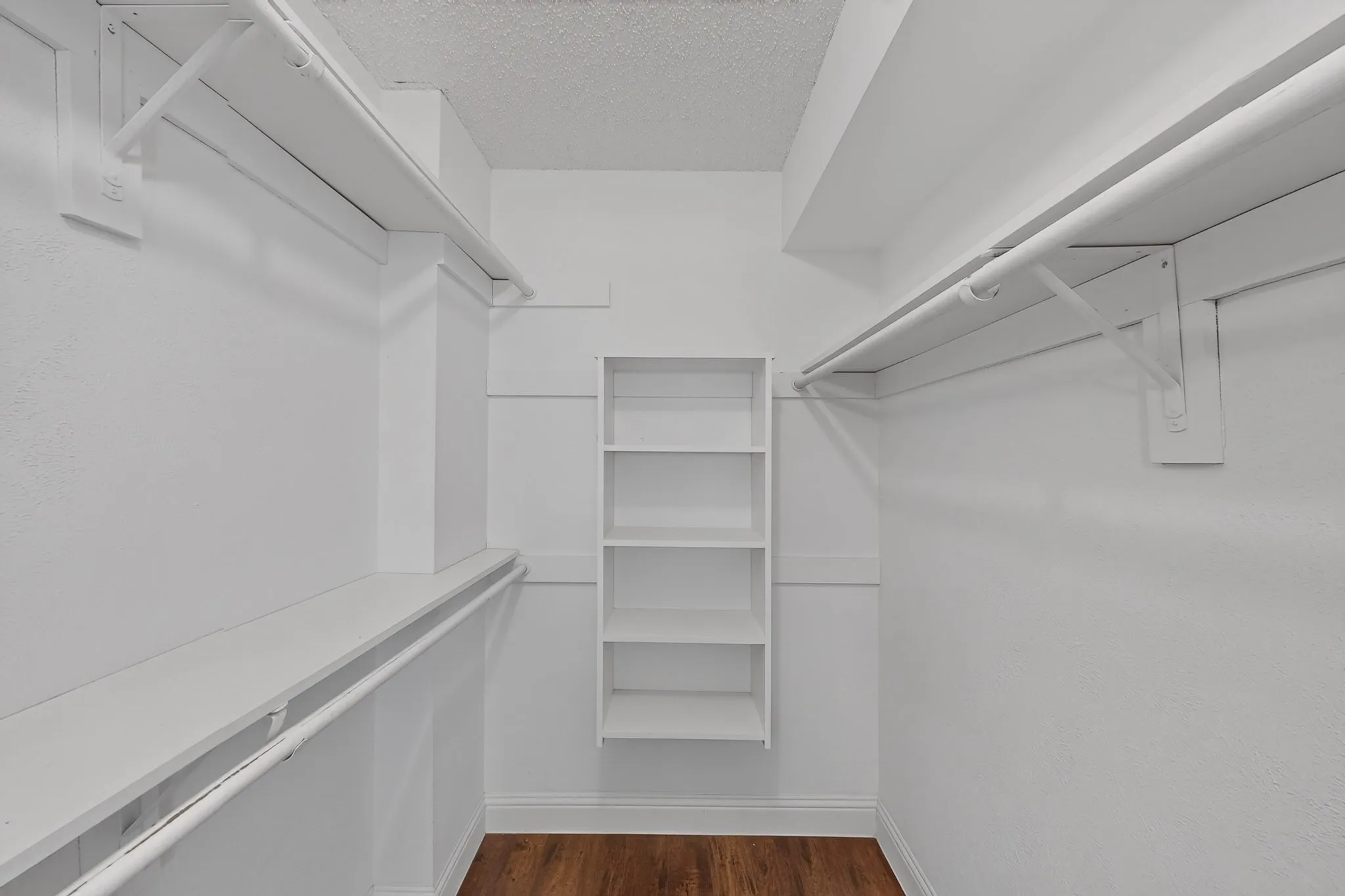 In Primary Bedroom White custom shelving, hanging rods, and wood-finish flooring