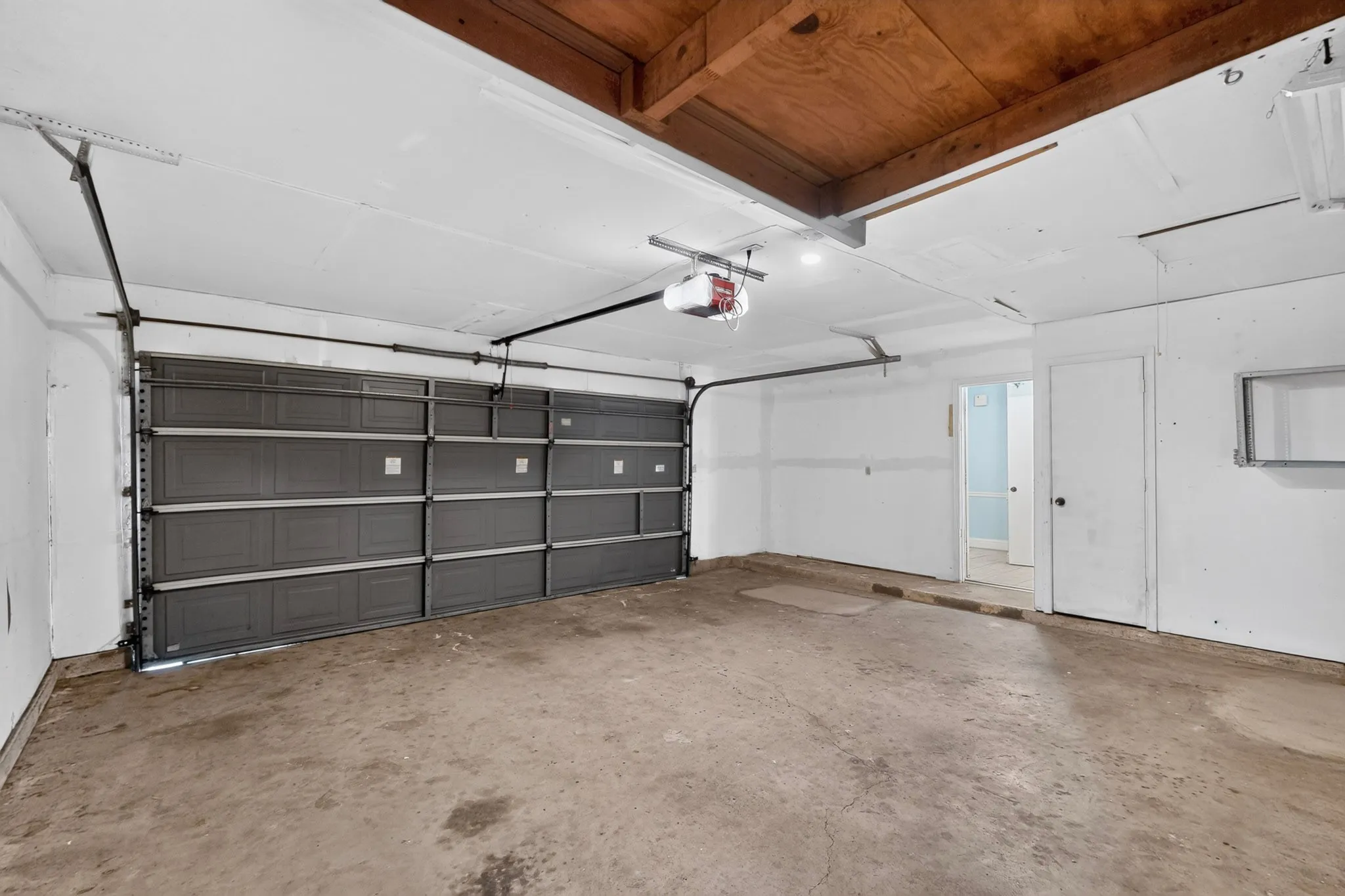 Spacious front facing oversized 2 car garage featuring a paneled overhead door, exposed wood ceiling, and concrete flooring