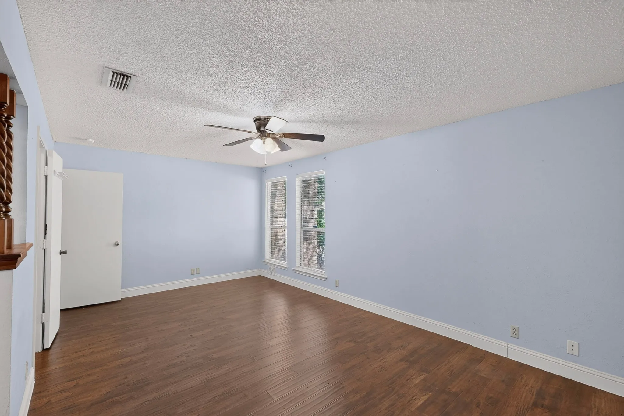 Spacious room featuring wood-finish flooring, light blue walls, and two multi-paned windows