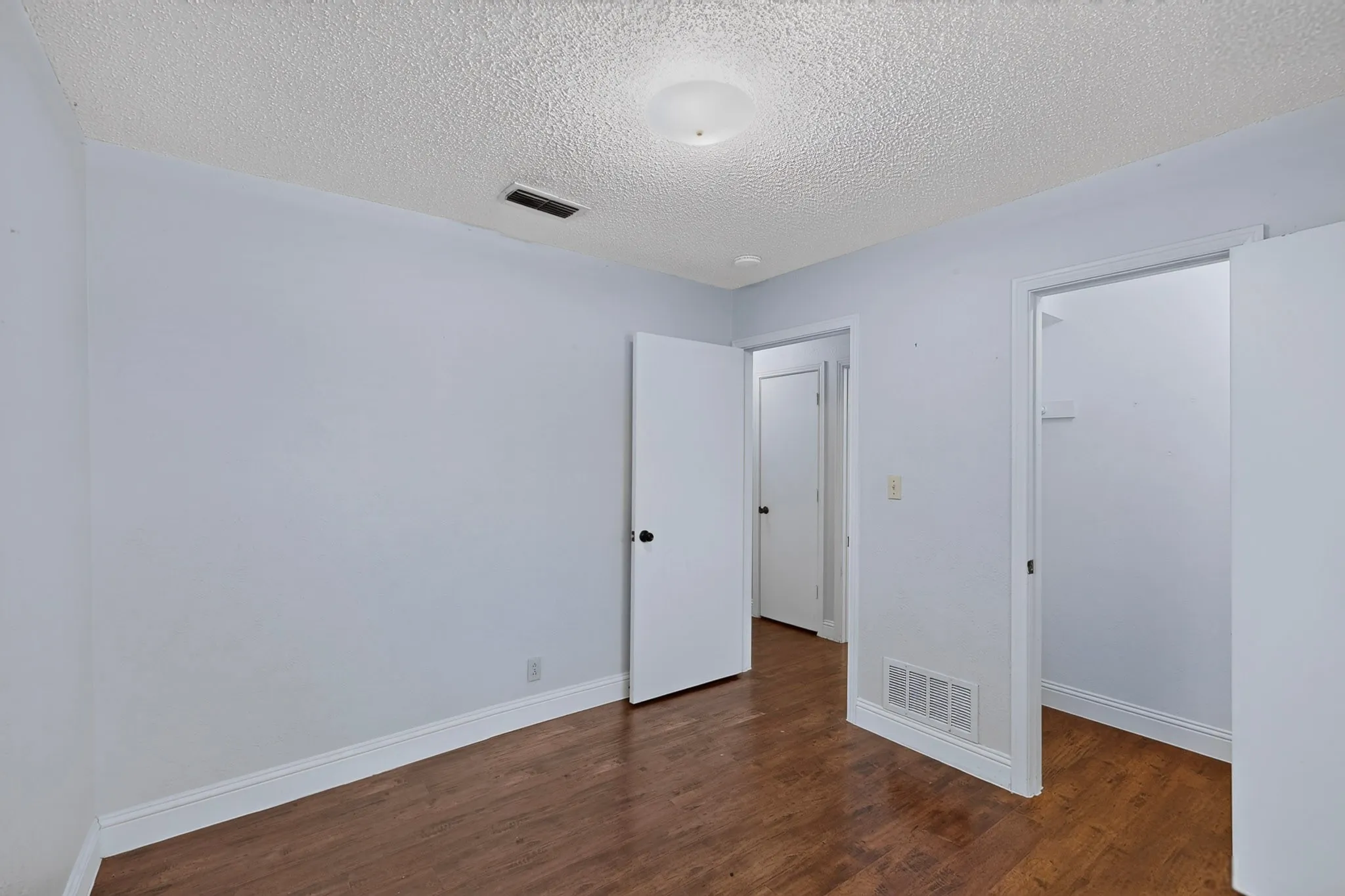 Wood-finish flooring with light-toned walls and white trim and walk in closet