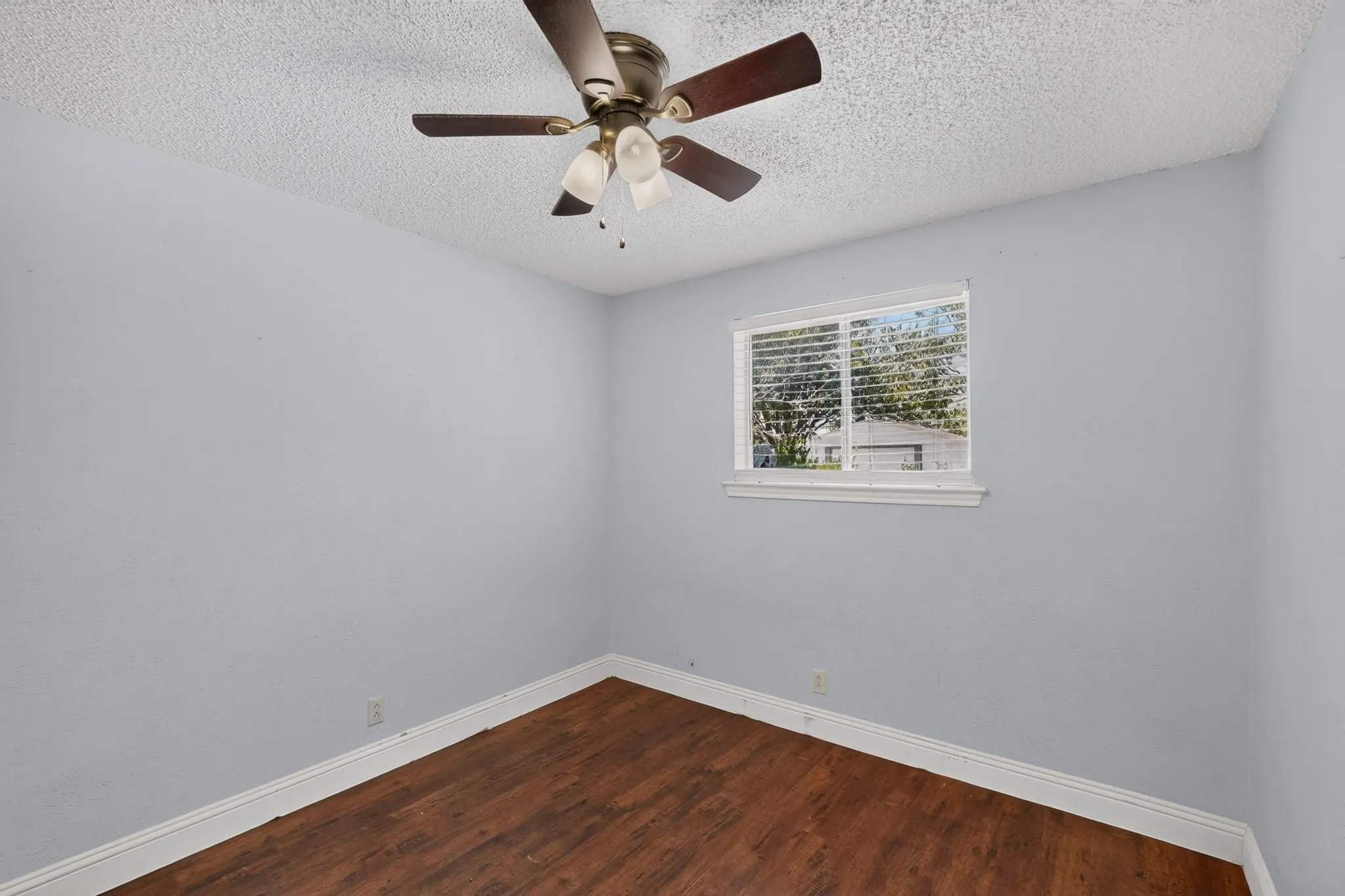Wood-finish flooring, white trim, a window with blinds, and a ceiling fan with integrated lighting