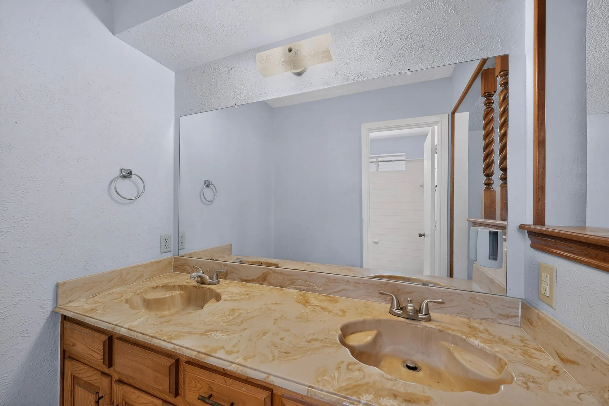 Dual integrated sinks with a natural stone countertop, wood cabinetry, and a large wall-mounted mirror