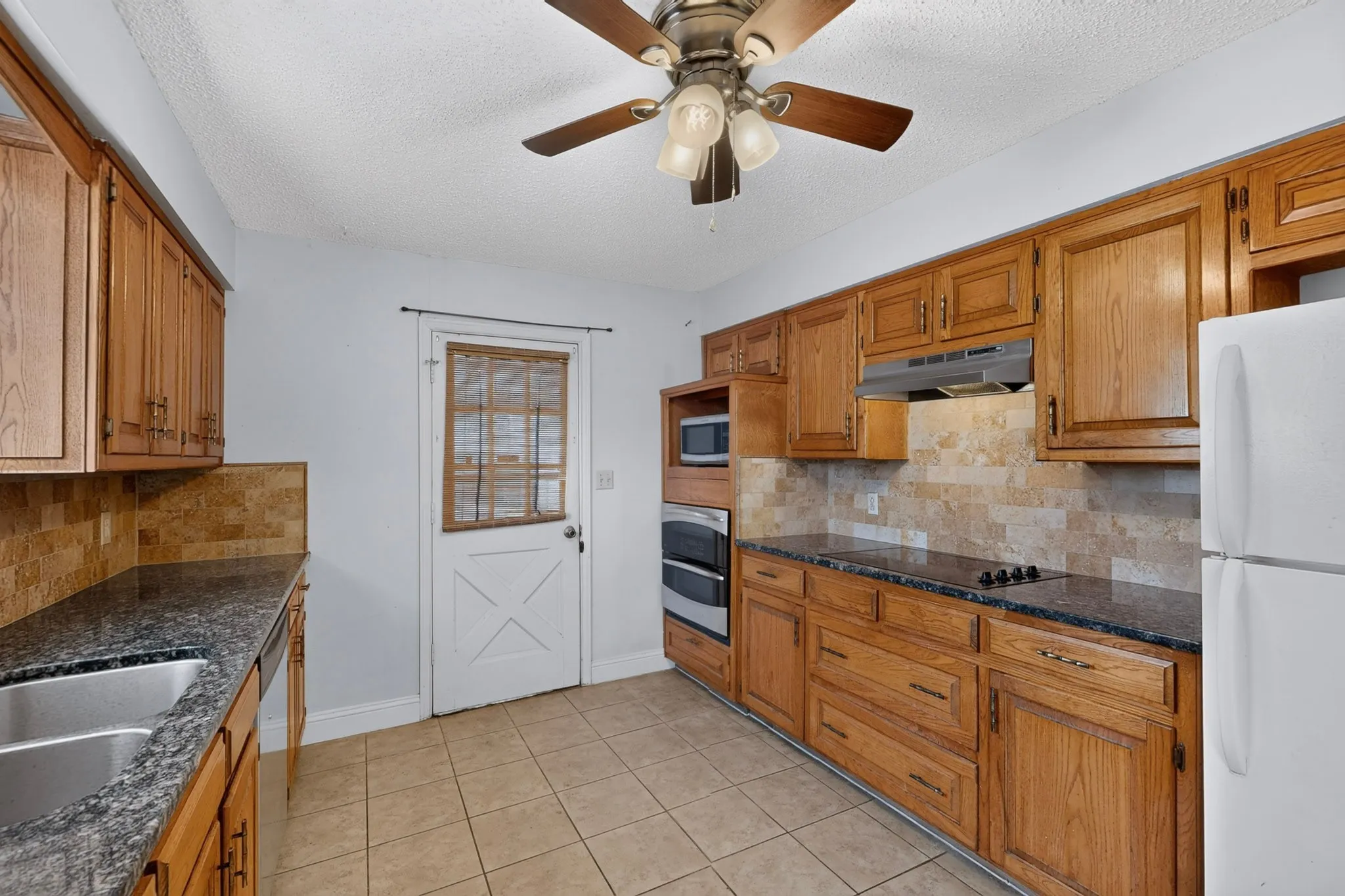 Wood-finish cabinetry, granite-style countertops, tile flooring, built-in double oven, and a ceiling fan