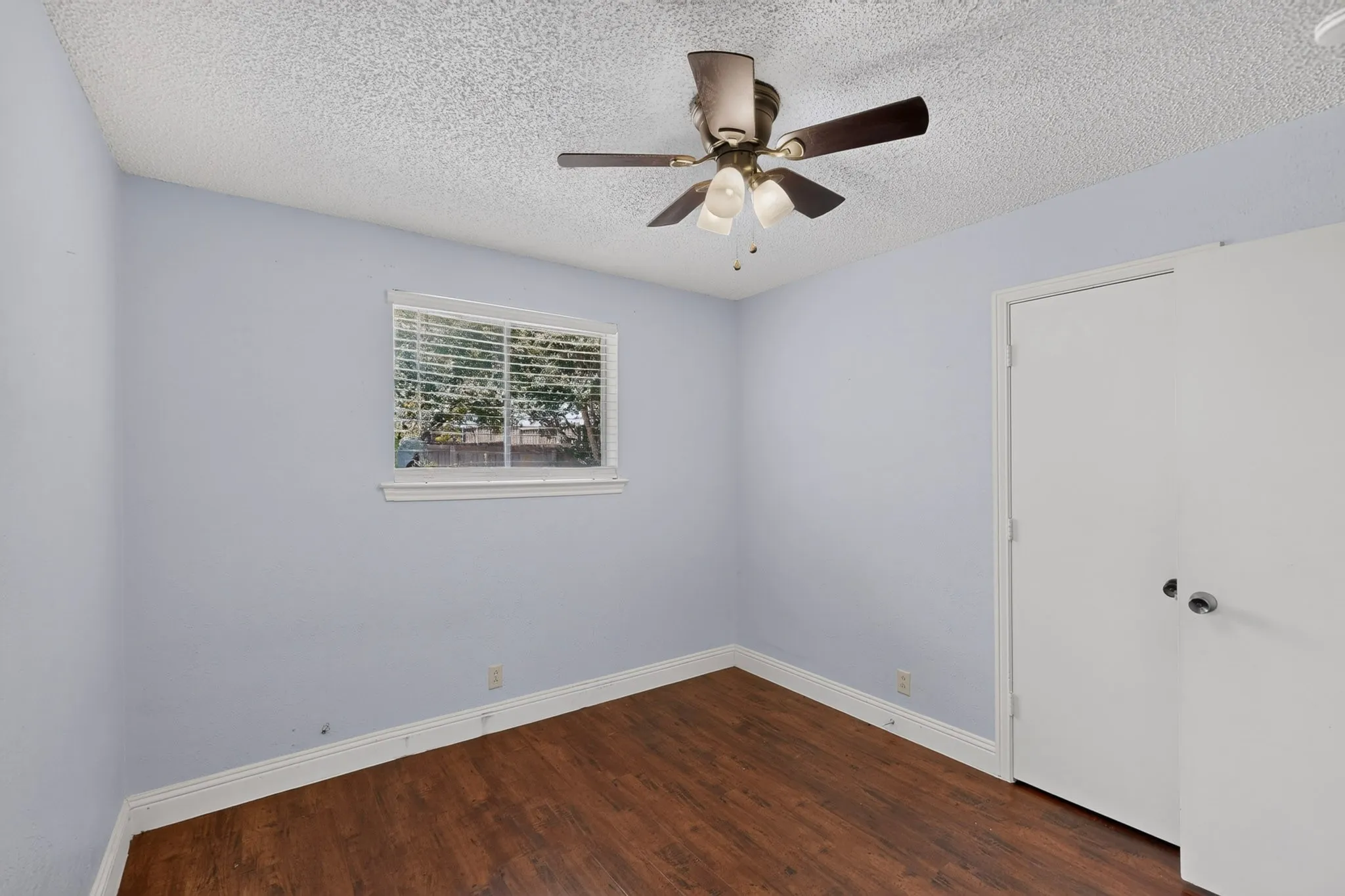Wood-finish flooring, white trim, a window with blinds, and a ceiling fan with integrated lighting