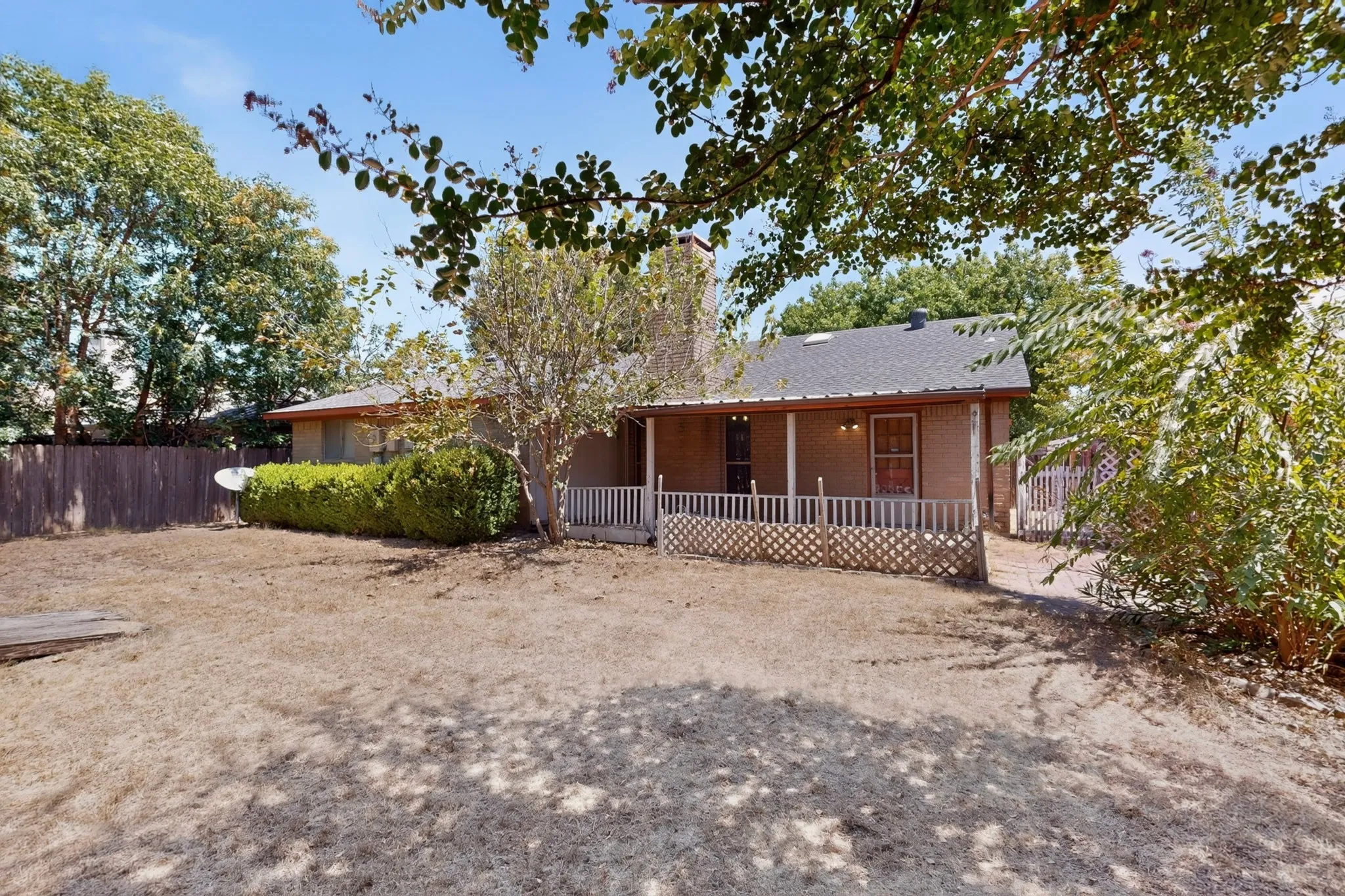 Expansive green lawn, covered patio, brick exterior, wood privacy fence, and mature trees