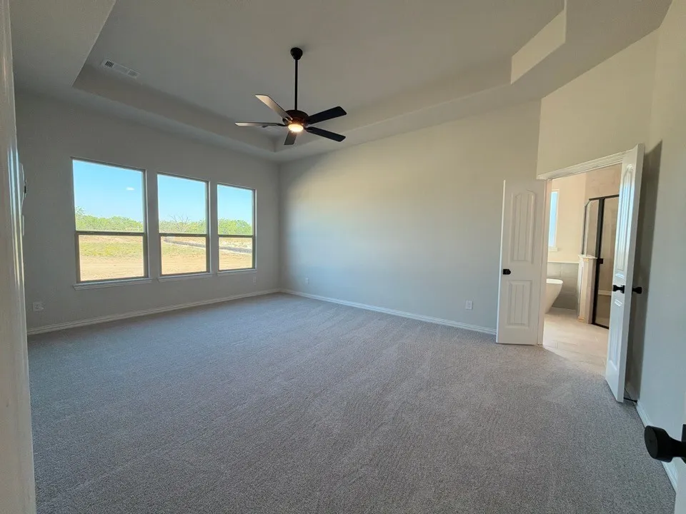 Recessed ceiling with a contemporary ceiling fan, light gray carpeting, and a series of three windows