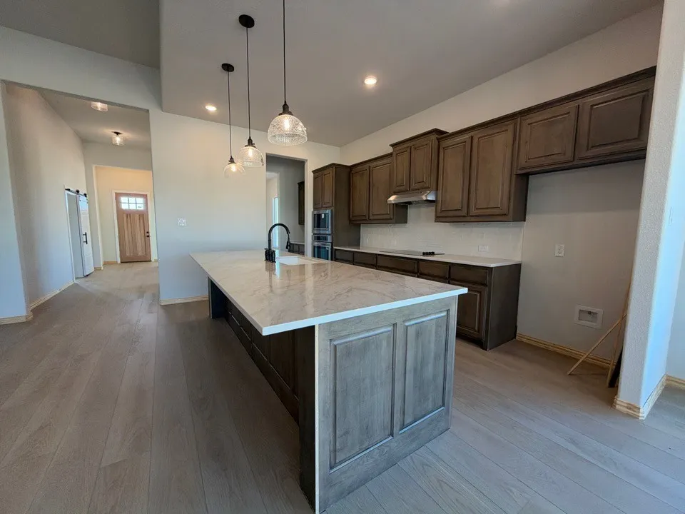 Kitchen featuring a large island with a light-colored countertop, dark wood-finish cabinetry, and pendant lighting