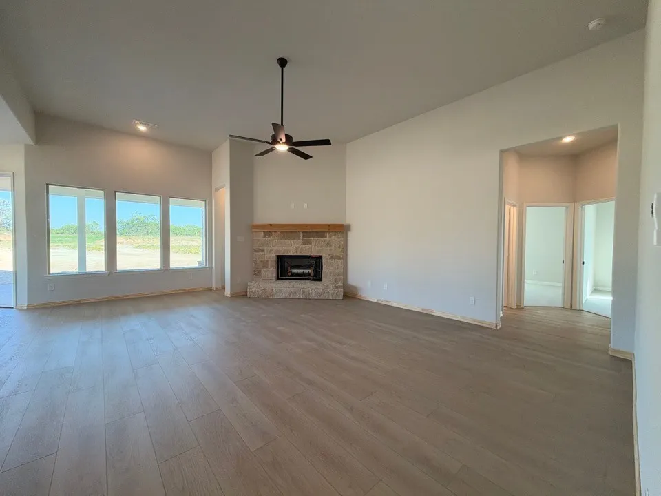 Spacious room with wood-finish flooring, a stone fireplace with a wood mantle, vaulted ceiling, and recessed lighting
