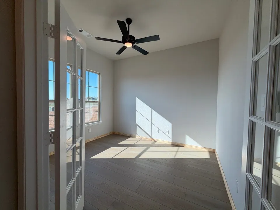 Room featuring wood-finish flooring, two windows, and a ceiling fan with integrated lighting