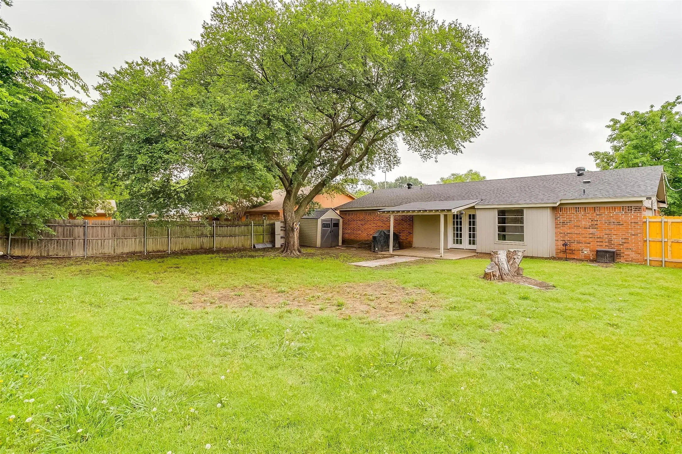 Expansive grass lawn with mature trees, wood privacy fencing, and a detached storage shed